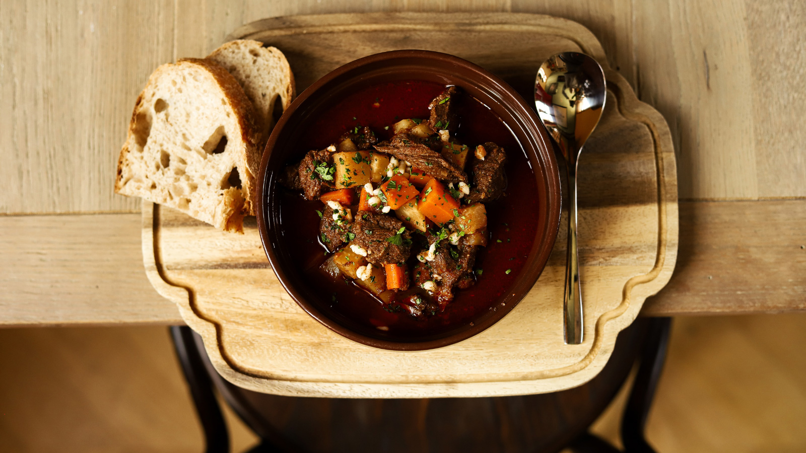 Gulyásleves gazdagon kenyérrel és kanállal, fa tálalódeszkán