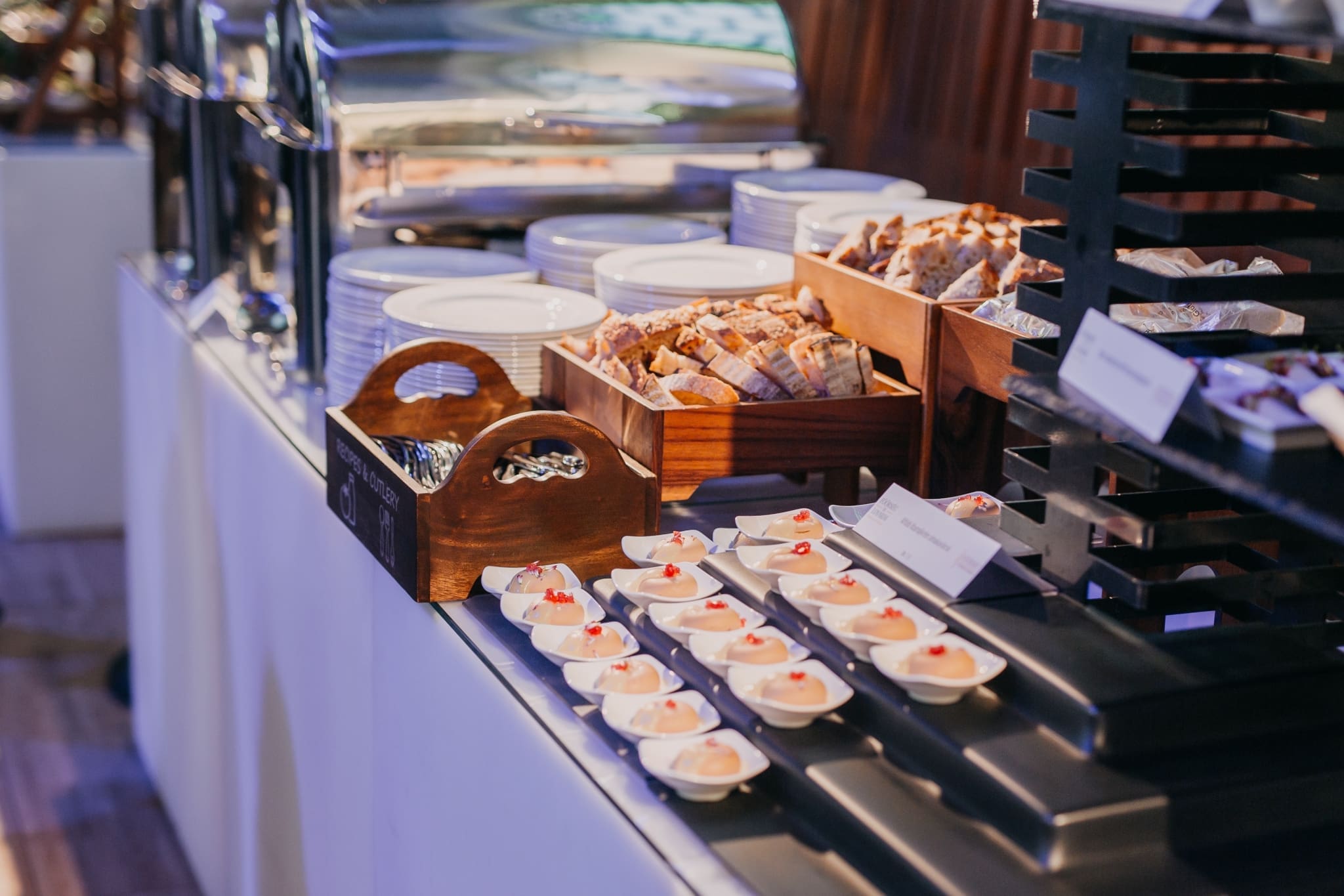 Catering asztal melegen tartó tálakkal, tányérokkal, evőeszközökkel és kenyeres kosarakkal